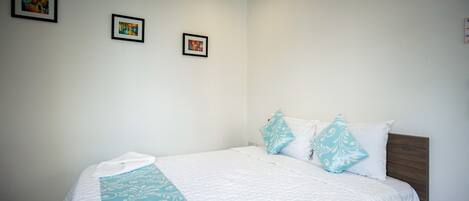 A neatly made bed with a white quilt and blue accents, a wooden headboard, and three framed pictures on the wall.