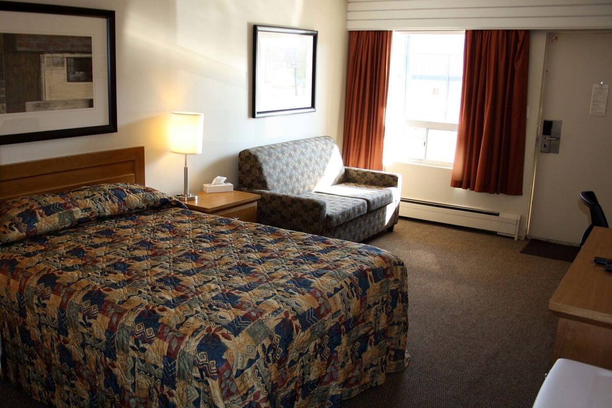 A hotel room with a large bed, a chair, a desk, a lamp, and a window with curtains.