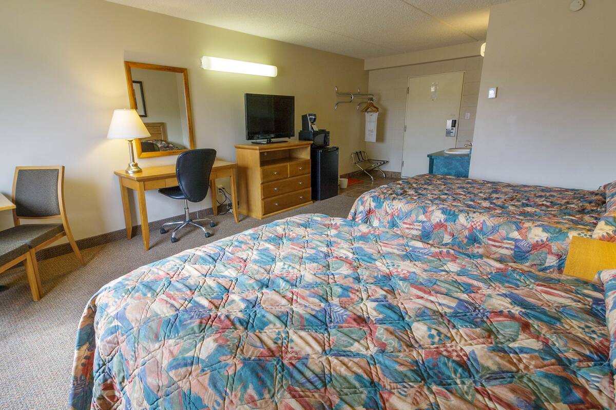A hotel room with a bed, a desk with a chair, a television, a dresser, and a bathroom.