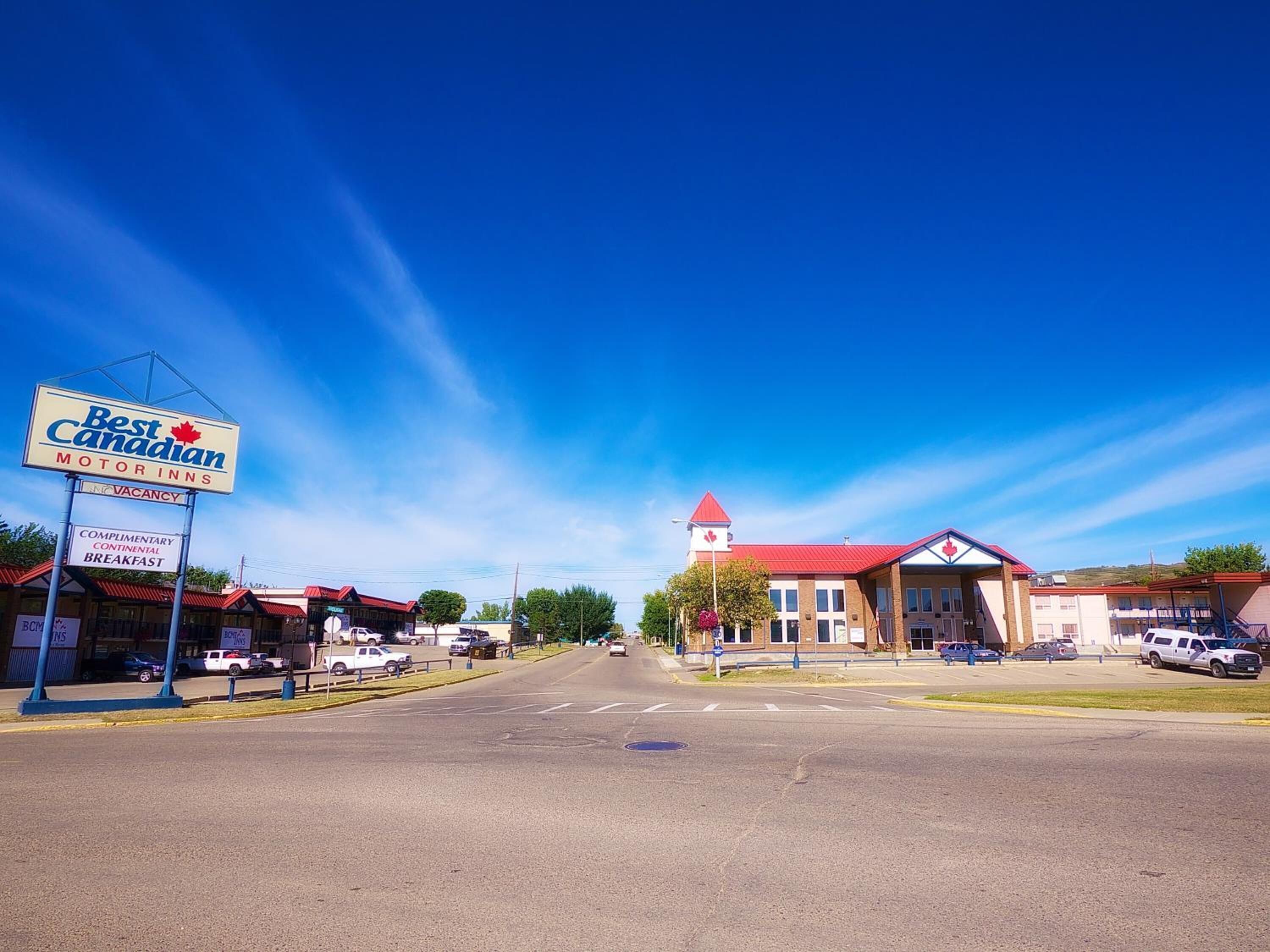 Un letrero de Best Canadian Motor Inns, un edificio con techo rojo y un cielo azul despejado.