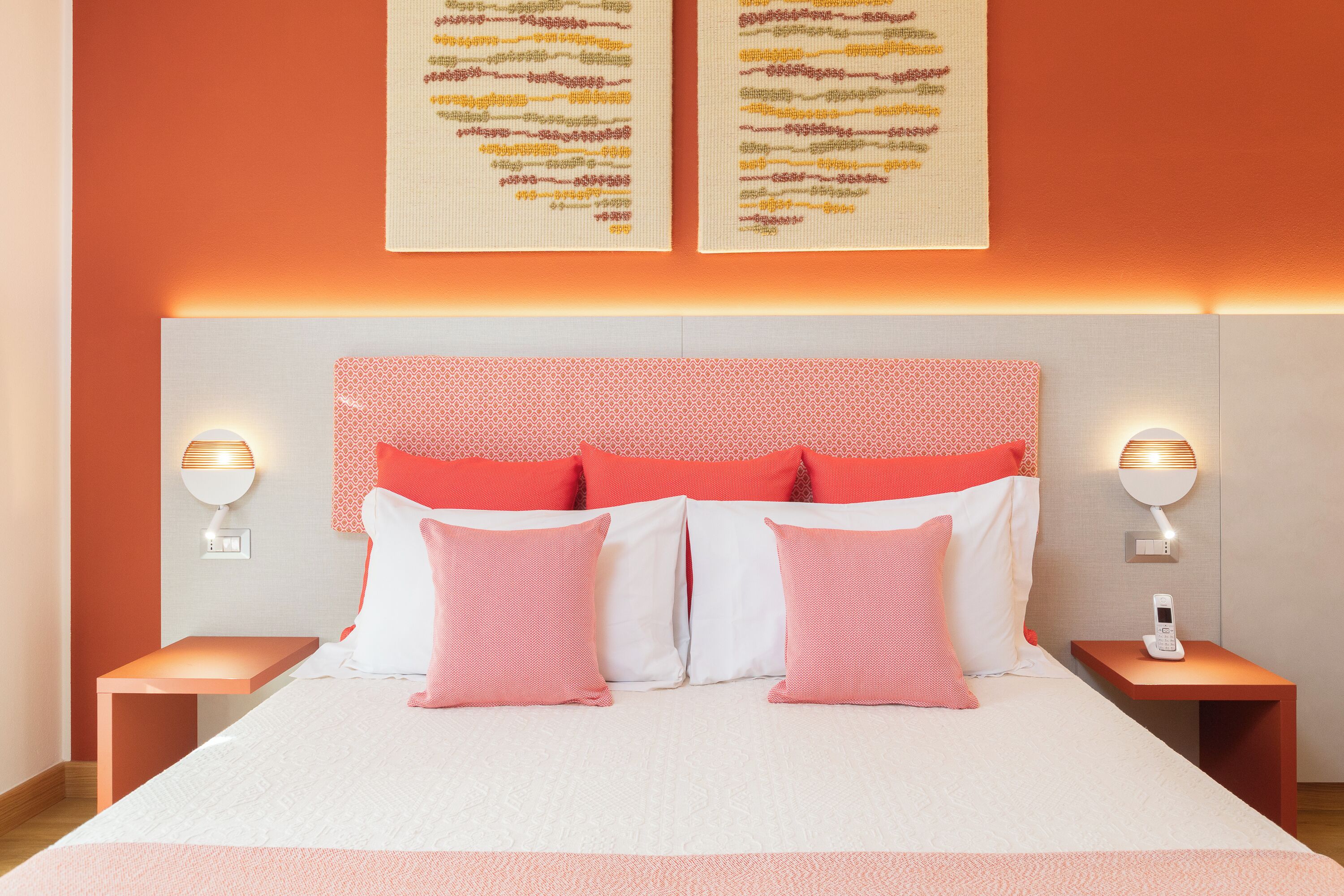 Une chambre d’hôtel bien aménagée, avec un grand lit, deux tables de chevet et des lampes fixées au mur.
