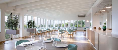 A spacious dining area with multiple tables and chairs, large windows, and a high ceiling.