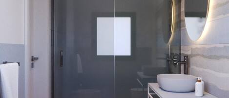 A modern bathroom with a glass shower enclosure, a round sink, a toilet, and a vanity with a mirror.