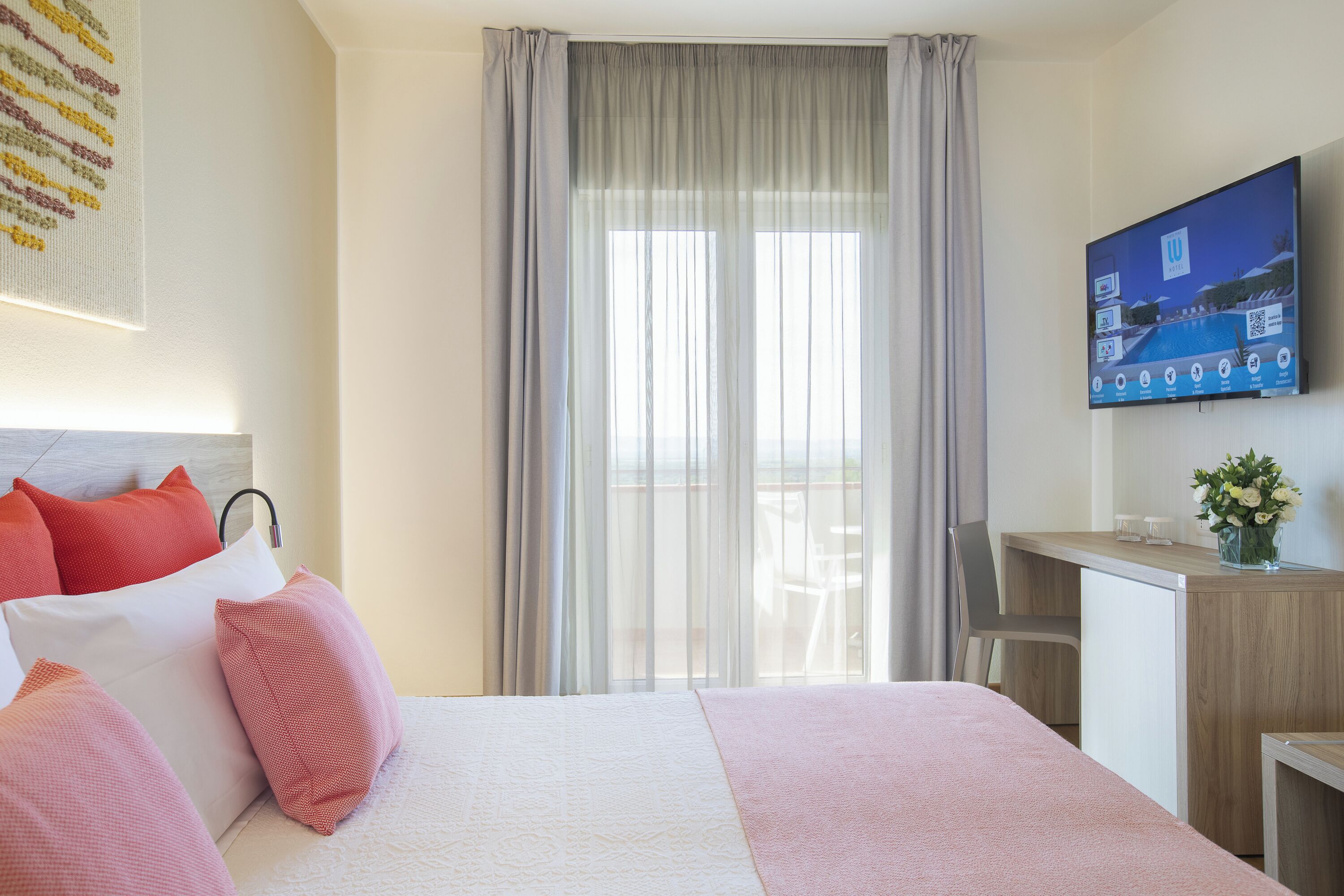 A hotel room with a bed, a desk, a TV, and a view of the outdoors.