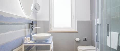 A modern bathroom with a large white sink, a glass shower enclosure, and a window above the toilet.