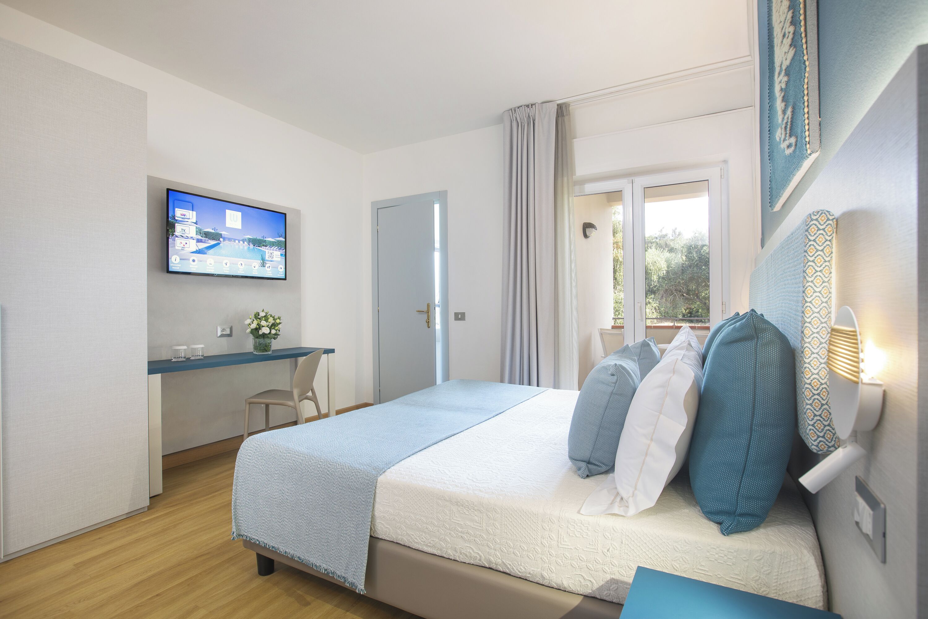 A bedroom with a bed, a desk, a television, and a window with curtains.