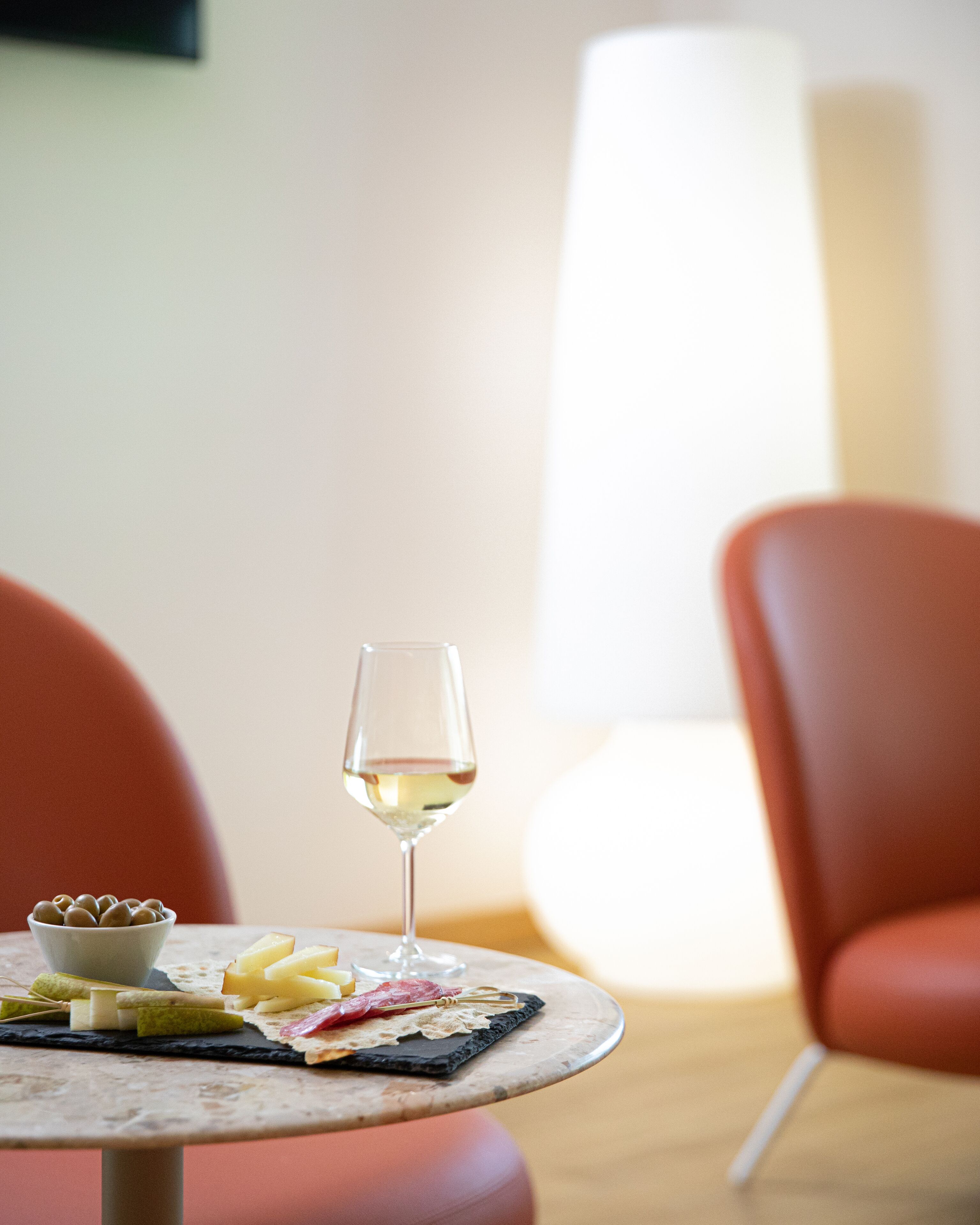 Una mesa de mármol con una copa de vino blanco, un cuenco de frutos secos y queso.