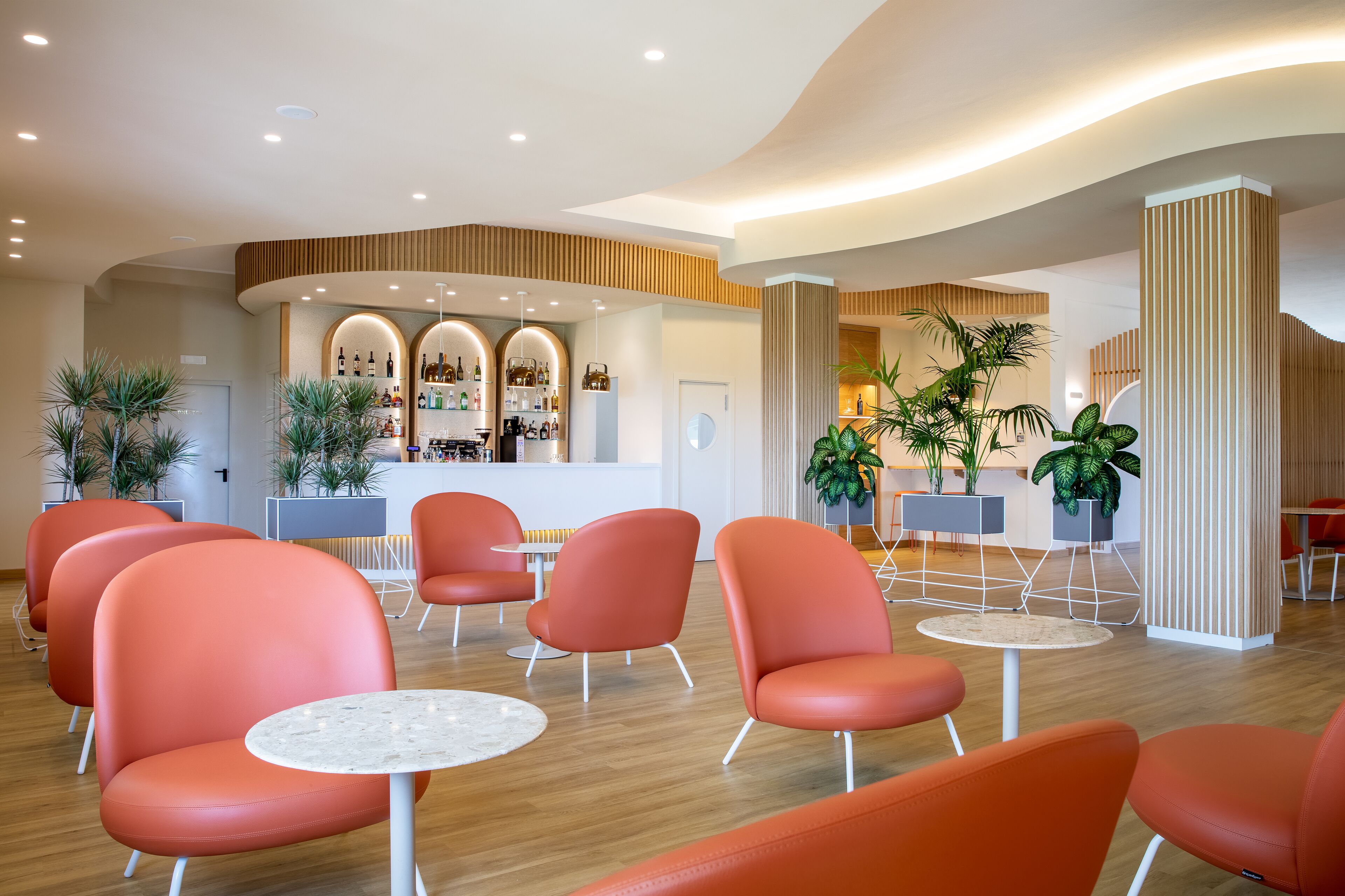 Una hall moderna con poltrone arancioni, un'area bar e piante in vaso.