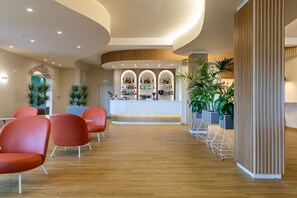 A reception area with a curved ceiling, wooden paneling, and a bar with shelves of bottles. There are red chairs and potted plants. - Lu' Hotel Porto Pino (Sant'Anna Arresi)