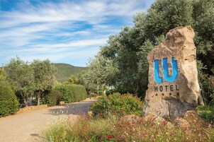 A large rock sign with 'PORTOPINO HOTEL' written on it, surrounded by greenery and a road.