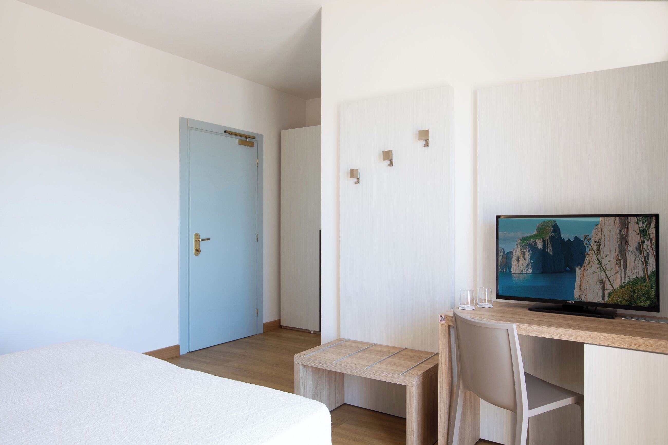 A hotel room with a bed, a desk with a computer monitor, and a small table.