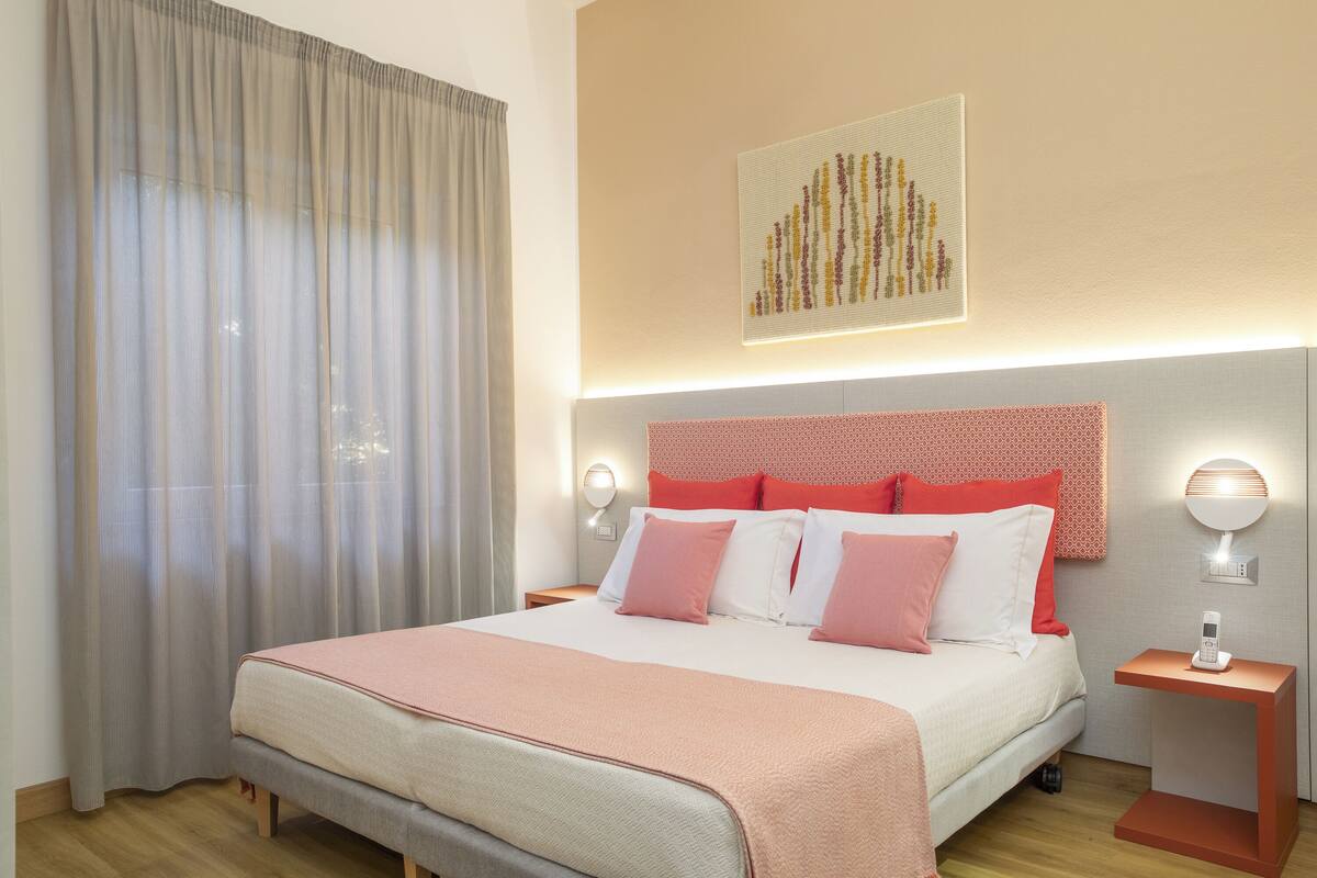 Ein Hotelzimmer mit einem großen Bett, einem Kopfende mit Muster, einem Nachttisch mit Lampe und einem Wandbild.