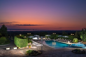 Zona de piscina con sillones de descanso y sombrillas, rodeada de follaje y vistas al paisaje.