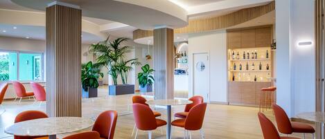 A modern interior with round tables and orange chairs, wooden accents, and a bar area with bottles.