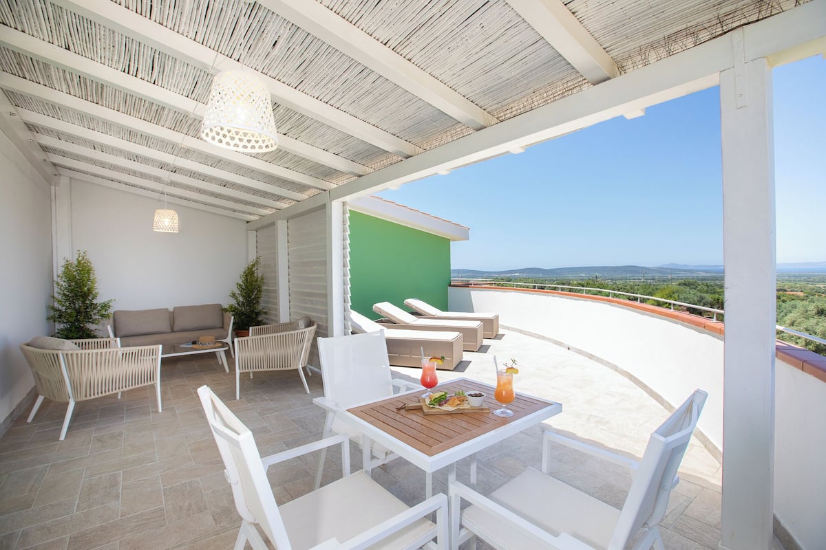 Eine Terrasse mit weißer Möbel, einem Tisch mit Getränken und Blick auf die Landschaft.