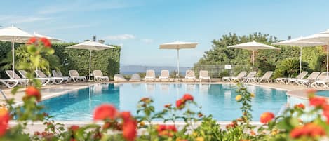 A pool with lounge chairs and umbrellas, surrounded by greenery.