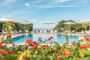 Une piscine entourée de verdure, avec des chaises longues et des parasols.