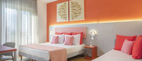 Une chambre d’hôtel avec un lit, un bureau et une chaise. Il y a deux appliques murales et une fenêtre avec des rideaux.