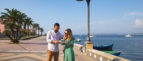 A couple standing on a waterfront promenade with a clear view of the sea and boats.