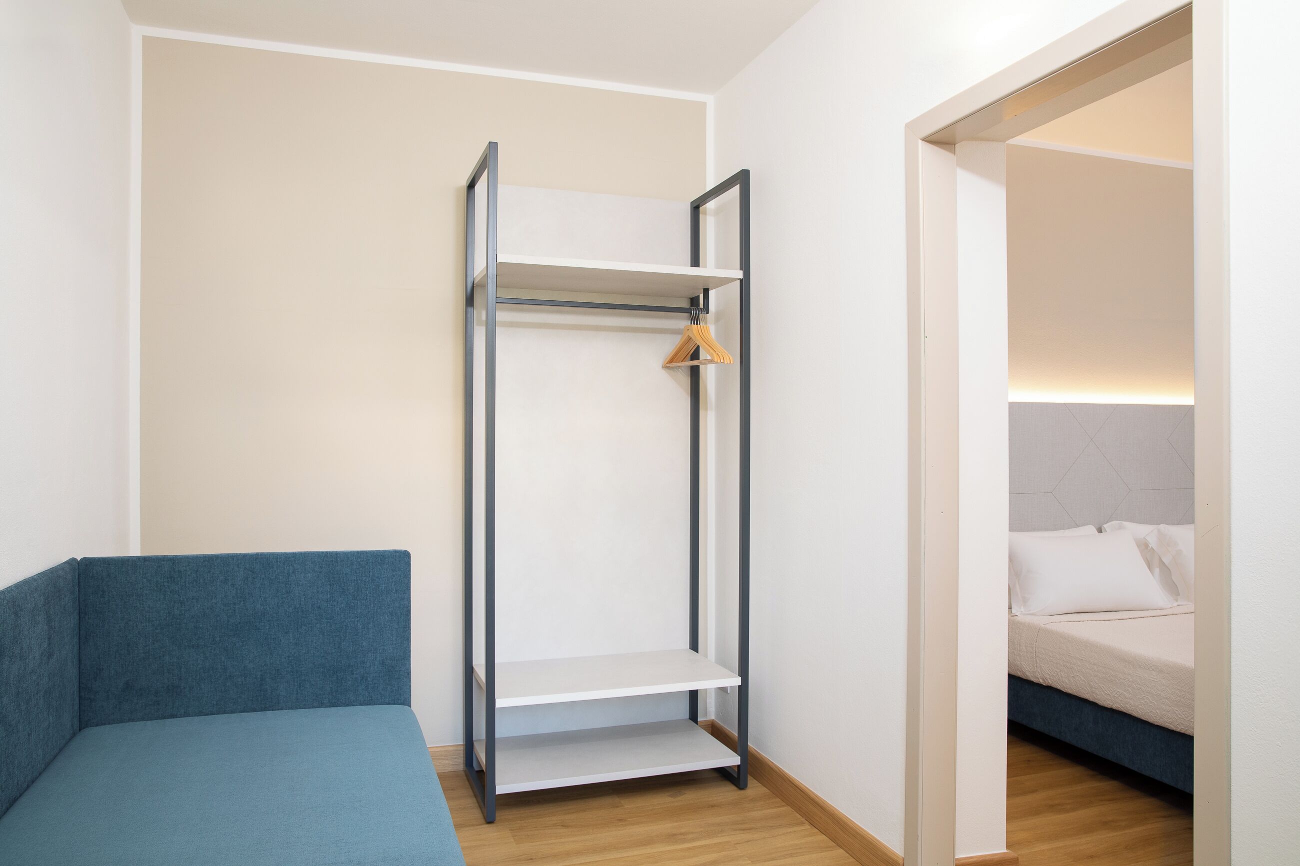 A room with a bed, a blue sofa, and a metal shelving unit with a wooden hanger.