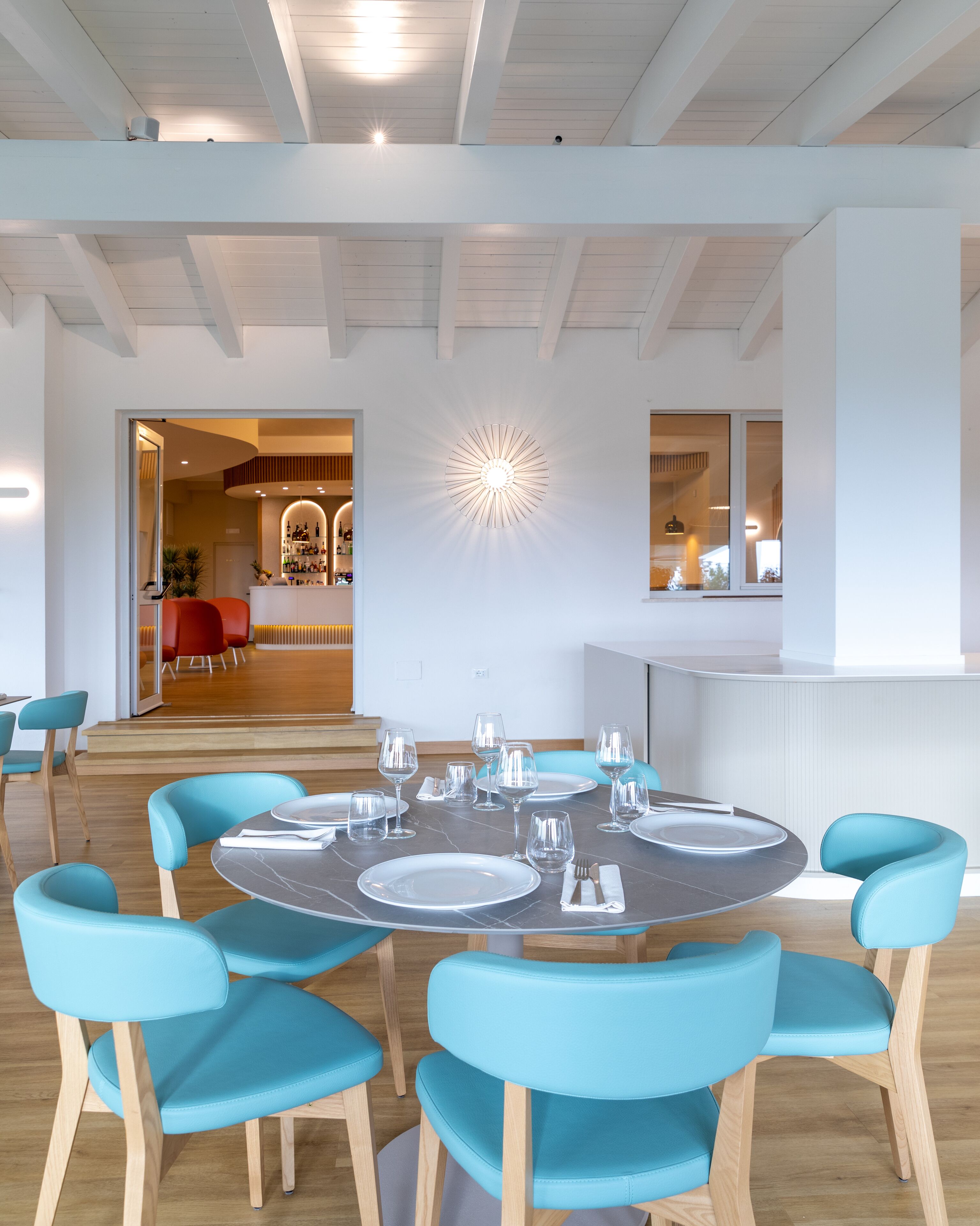 Un comedor moderno con una mesa redonda dispuesta para seis comensales, rodeada por seis sillas color aguamarina. Se observa una lámpara de techo original sobre la mesa.
