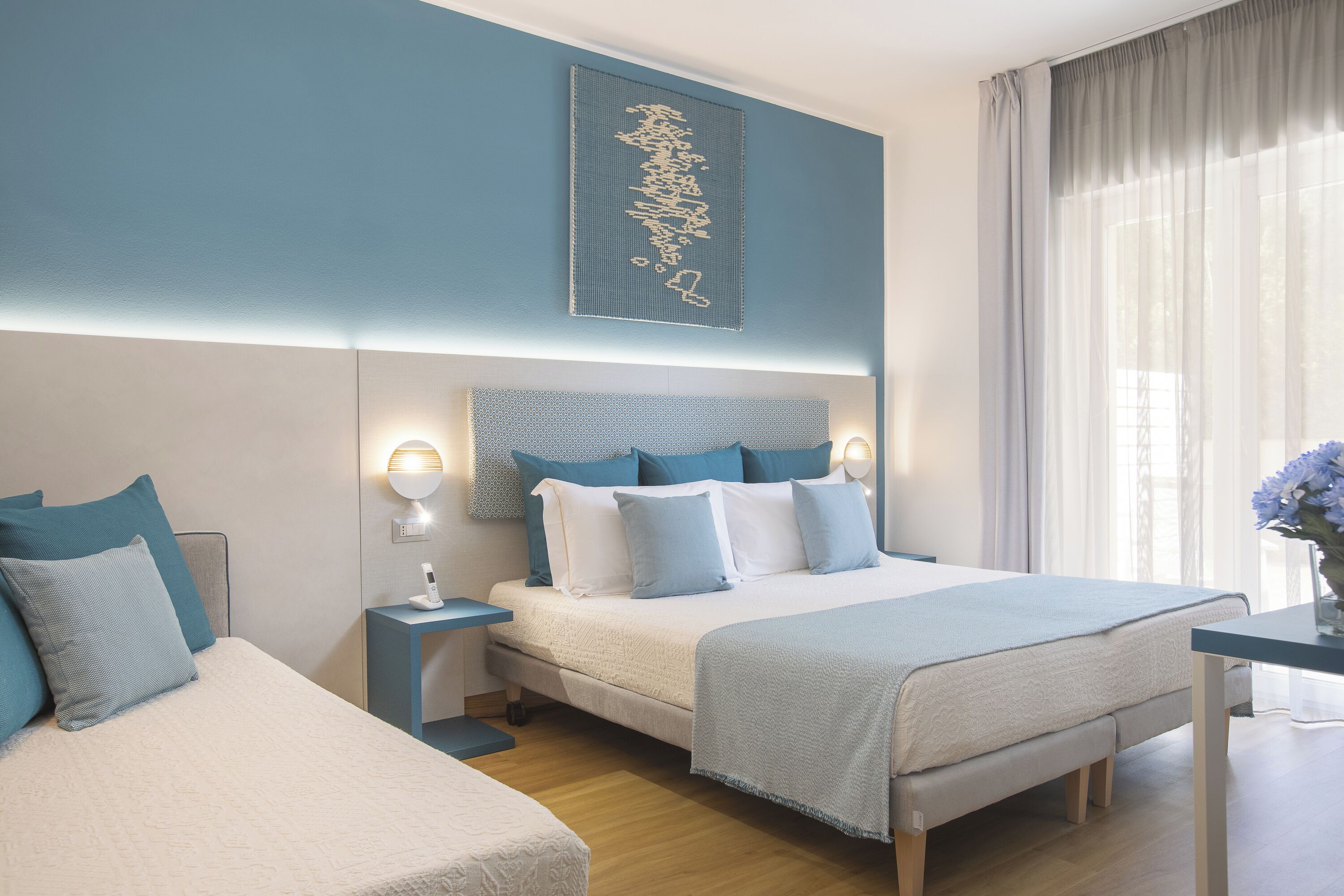 Une chambre d’hôtel moderne avec un grand lit, des tables de chevet, une petite table et un élément décoratif mural.