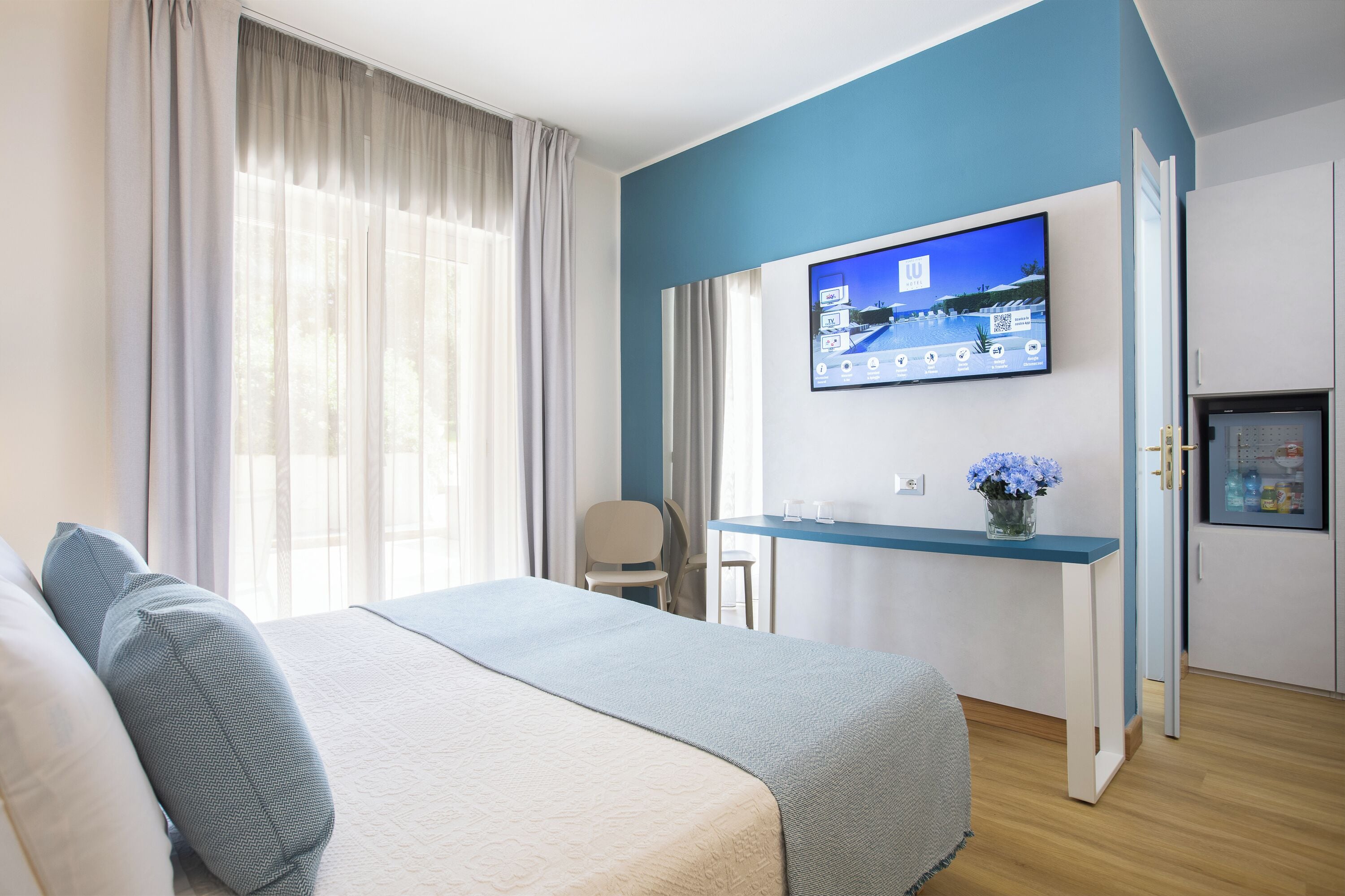 A hotel room with a bed, a desk, a TV, and a door.