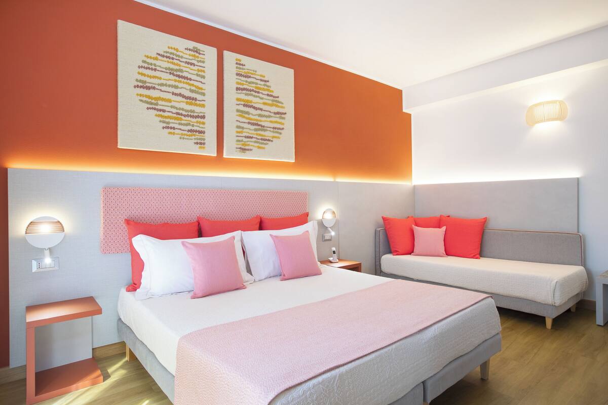 Ein modernes Schlafzimmer mit einem großen Bett, einer kleineren Couch, zwei Wandbildern, Nachttischlampen und einem Nachttisch.