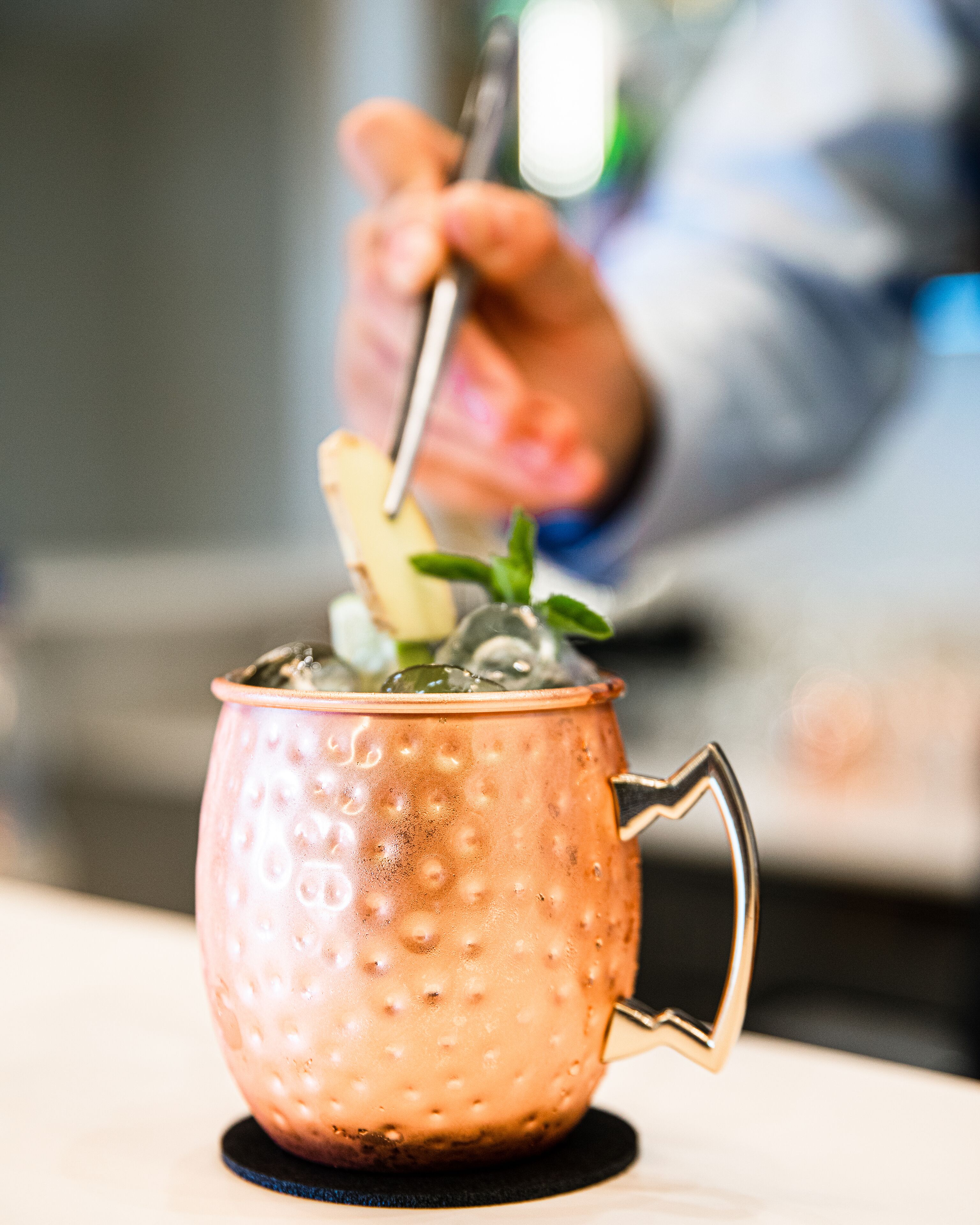 A copper mug with a handle, filled with ice and a drink, on a coaster.
