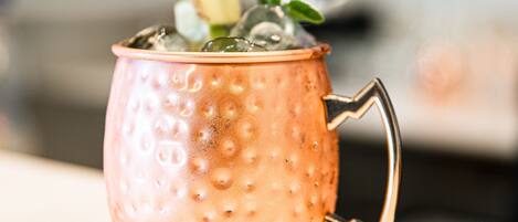 A copper mug with a handle, filled with ice and a drink, on a coaster.