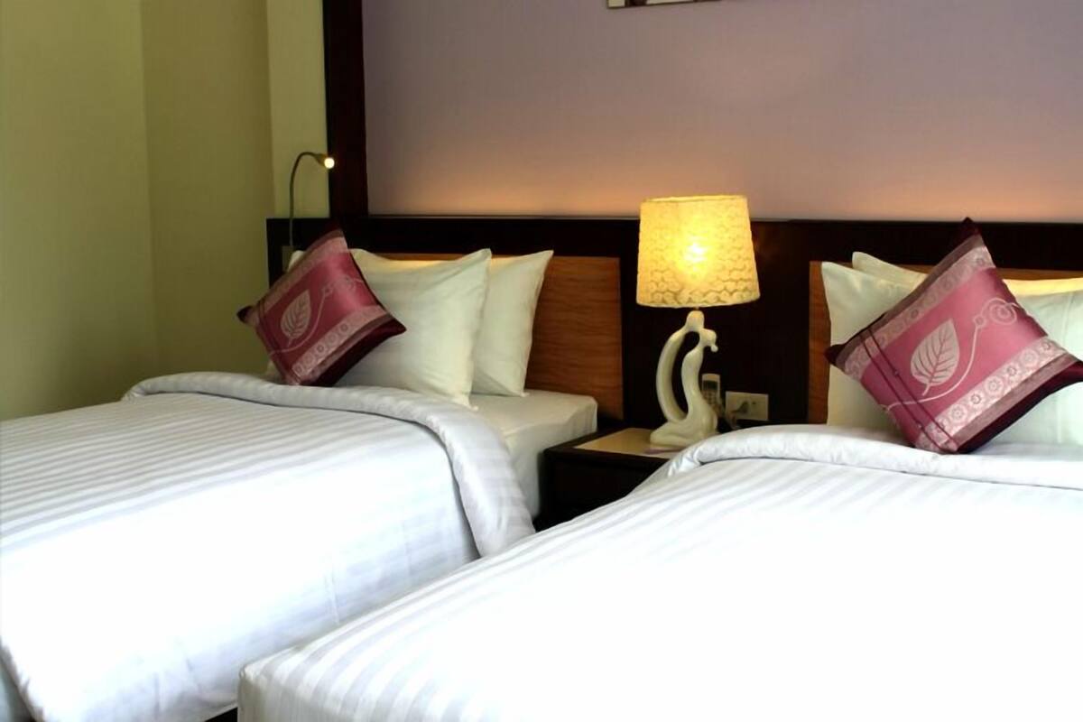 A hotel room with two beds, each with white bedding and decorative pillows. There is a nightstand with a lamp between the beds.