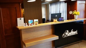 Un mostrador de recepción de hotel con encimera de madera, un reloj y un jarrón con flores amarillas.