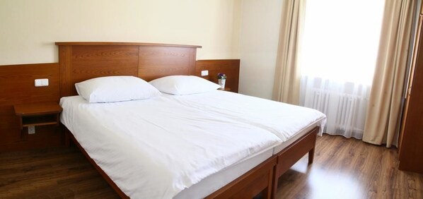 A neatly made bed with white linens in a room with wooden flooring and a wooden headboard.
