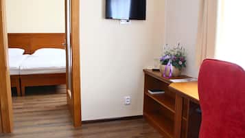 Een hotelkamer met een bed, een bureau met stoel, een aan de muur bevestigde televisie en een kleine plant op het bureau.
