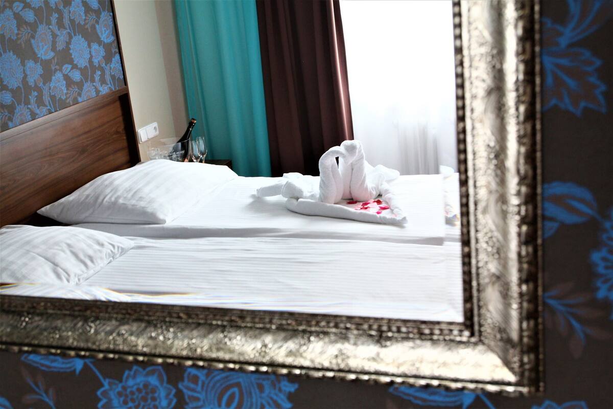 A neatly made bed with white linens, a bottle of champagne, and a folded towel on the side.