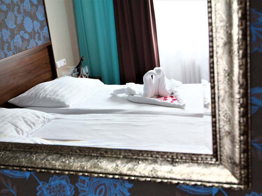 A neatly made bed with white linens, a bottle of champagne, and a folded towel on the side.