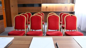 Un salón de conferencias con mesas de madera, sillas tapizadas en rojo y un mueble de madera con una lámpara.