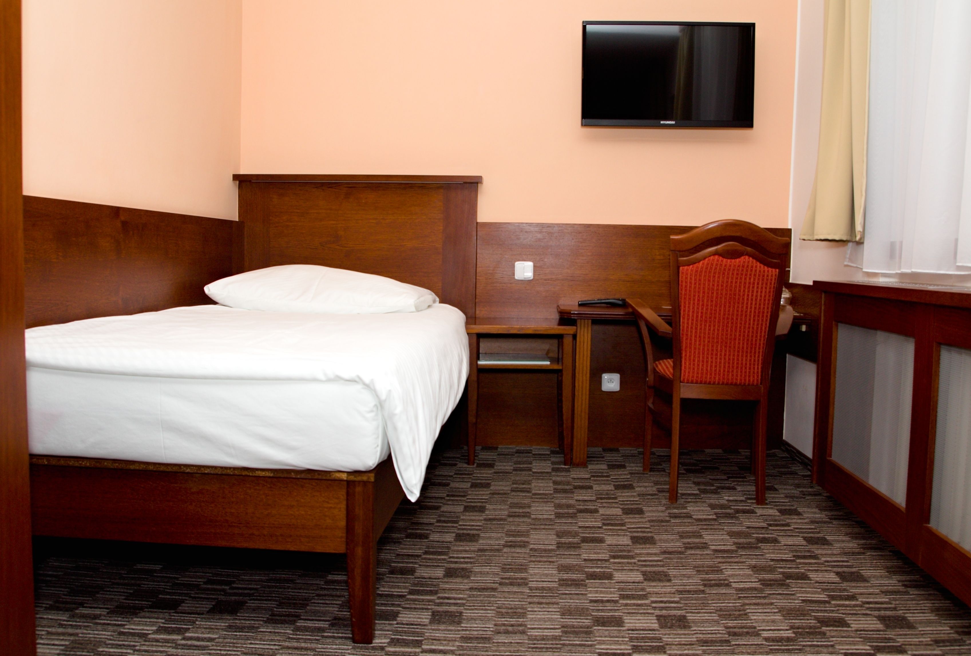 A hotel room with a bed, desk, chair, and a TV mounted on the wall.