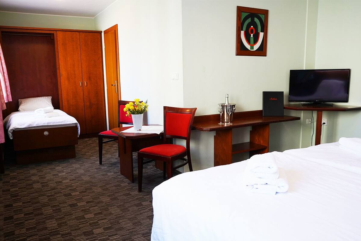A hotel room with a bed, a desk with a chair, a television, and a painting on the wall.