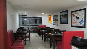 A restaurant with red upholstered booths and tables, a glass partition, and framed posters on the walls.