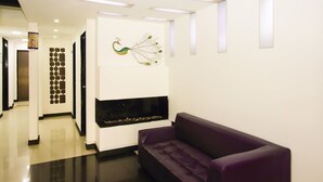 A modern lobby with a purple sofa, a wall-mounted peacock sculpture, recessed lighting, and a tiled floor.