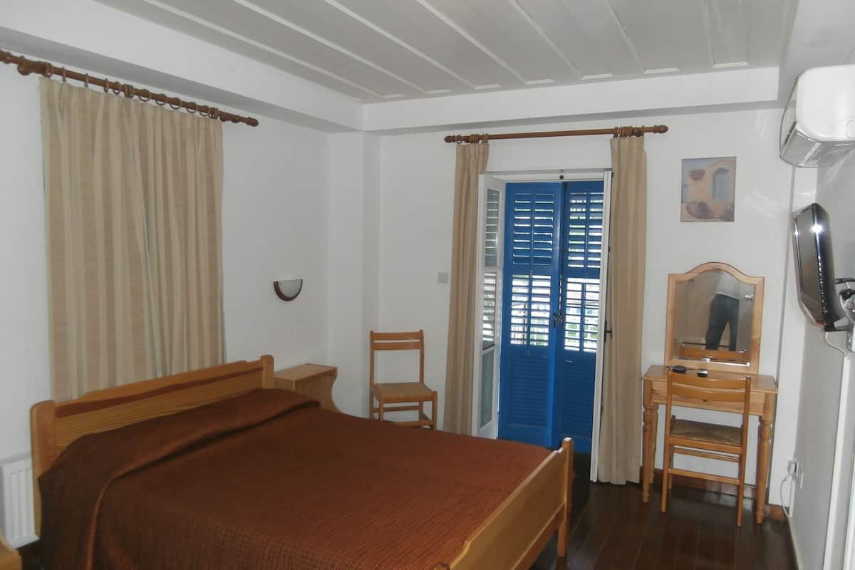 A bedroom with a bed, a chair, a desk, a mirror, and a blue door.