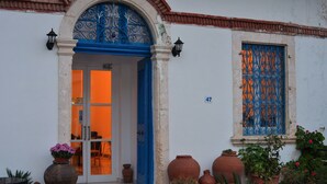 A building with a blue door and window, numbered 47, surrounded by potted plants and terracotta pots.