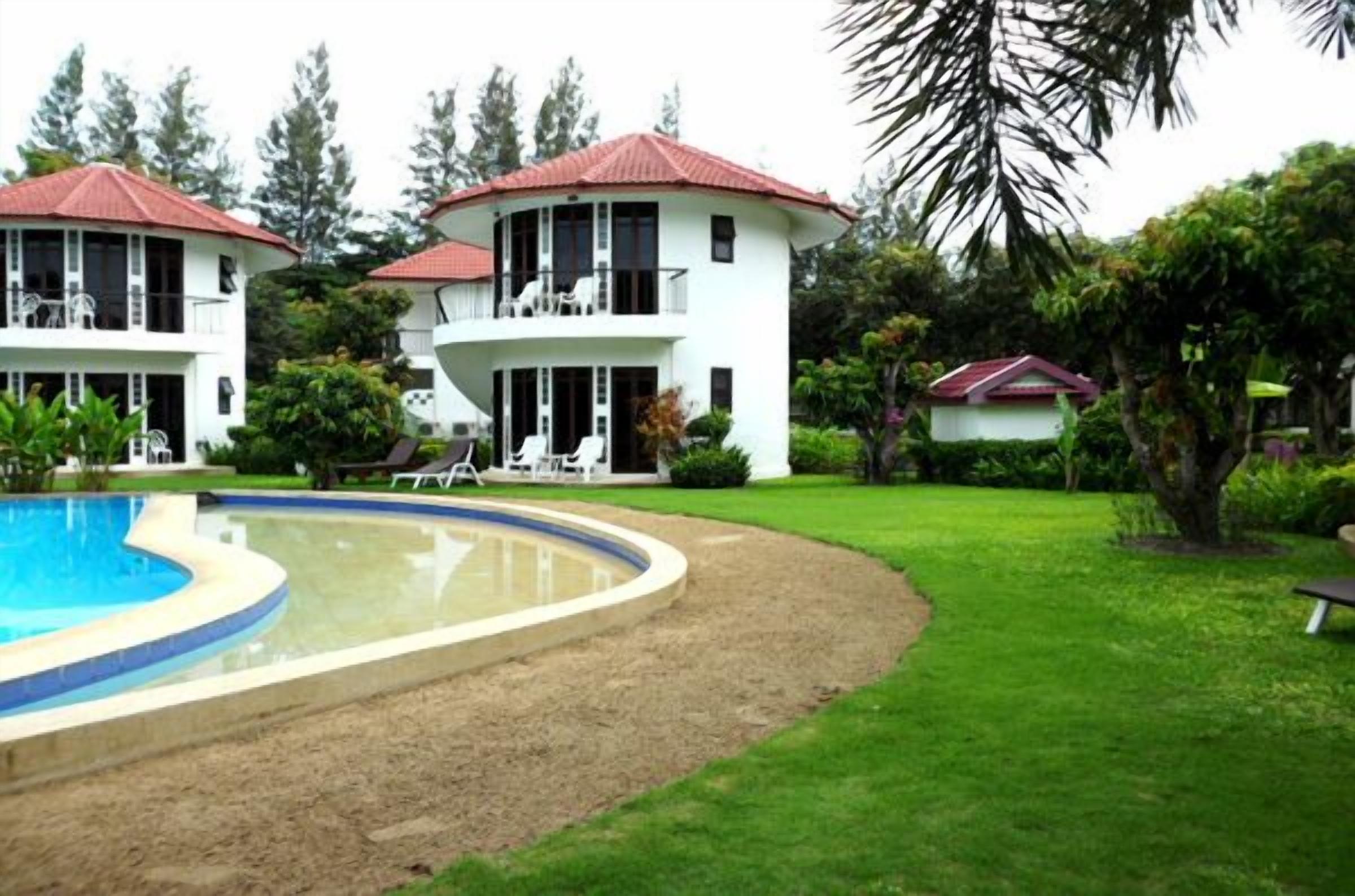 A two-story building with a pool, surrounded by lush greenery and palm trees.