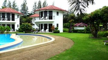 A two-story building with a pool, surrounded by lush greenery and palm trees.