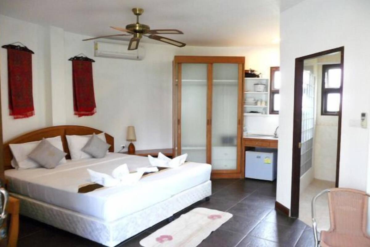 Une chambre à coucher comprenant un lit, un bureau, une chaise, une armoire et un ventilateur de plafond.