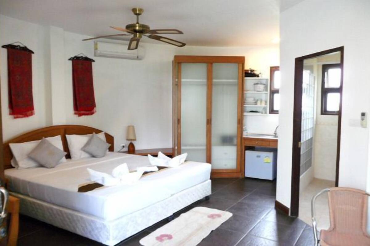 Une chambre à coucher comprenant un lit, un bureau, une chaise, un ventilateur de plafond et une armoire.
