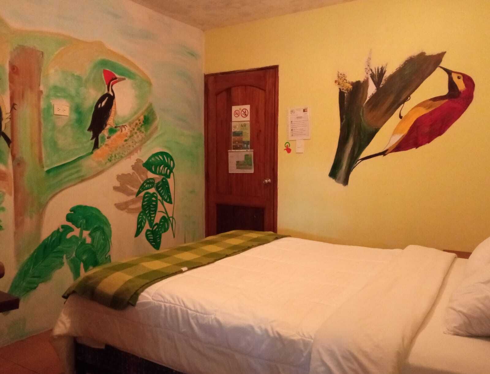 Una habitación con cama, puerta y paredes decoradas con pinturas de aves.