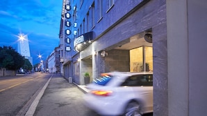 Hotel moderno con un letrero claro que dice "PARKING", entrada visible y vista de la calle con un coche estacionado.