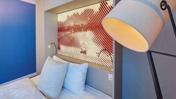 A modern hotel room with a bed, two pillows, a wall-mounted artwork, and a floor lamp.